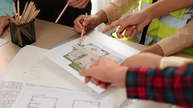 Smart architect and safety engineer discussion about building blueprint on table with architectural document, measurement tools and wooden block scatter around at modern office. Closeup. Delineation.
