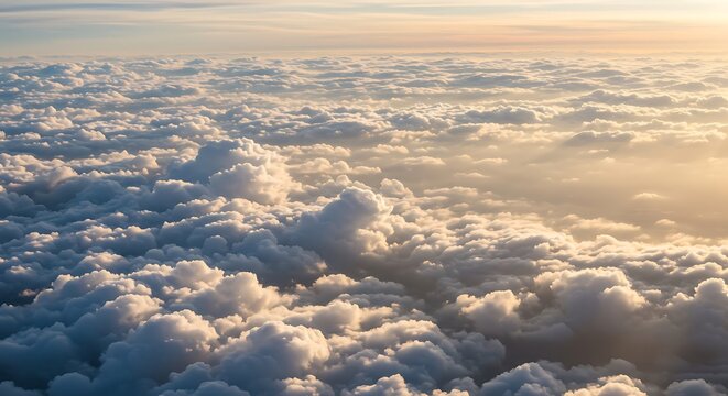 High-angle view of fluffy cumulus clouds illuminated by golden sunlight at sunrise or sunset.