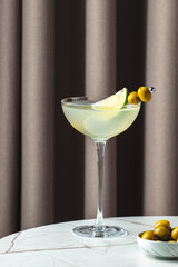 Refreshing Mexican martini served in a stylish glass with lime and green olives on a marble table