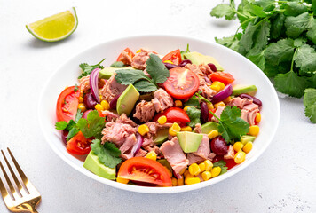 Mexican style salad with canned tuna, avocado, corn, red beans, cherry tomatoes and cilantro, white table background, top view