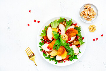 Autumn persimmon salad with grilled chicken fillet, pomegranate seeds, walnuts, oranges and lettuce, white table background, top view