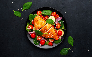 Healthy vegetable salad with grilled chicken, spinach, tomatoes, cucumber and red onion. Black table background, top view