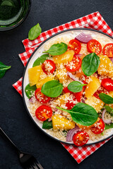 Gourmet vegan salad with couscous, tomatoes, onion, spinach and orange. Black background, top view