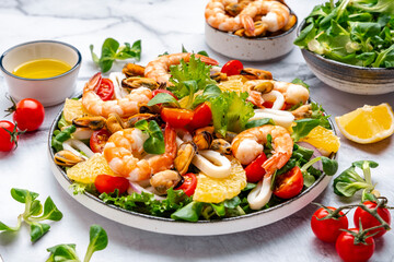 Gourmet seafood salad with shrimp, mussels, squid and oranges with lemon dressing, marble table, top view