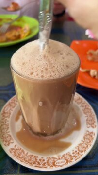 Traditional Indonesian Teh Tarik Being Stirred in a Vintage Glass