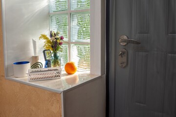 A bright and airy interior scene featuring a window, flowers, and an orange.