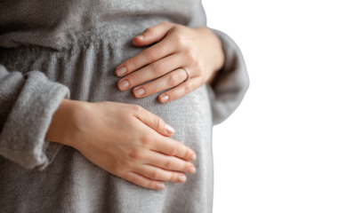 Close-up of a pregnant woman's belly, with her hands resting on her stomach against a white background. The focus is on her hand. Transparent background