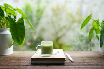 Matcha in a glass cup and philodendron notebook on rustic brown table