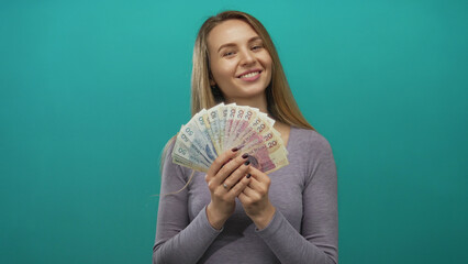 Young woman holding polish zloty banknotes against a vibrant green background, smiling confidently,...