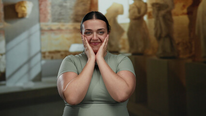 Woman smiling and clapping in modern museum with sculptures and soft lighting, showcasing joy and art appreciation in an indoor cultural setting.