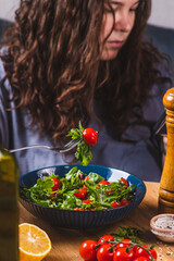 A woman eats a salad of arugula and cherry tomatoes