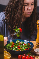 A woman eats a salad of arugula and cherry tomatoes