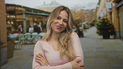 Woman with crossed arms on outdoor shopping street smiling at camera; confidence optimism...