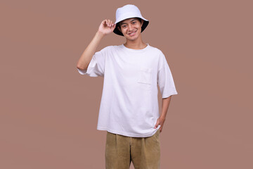 Standing Asian Man Wearing a White Bucket Hat and T-Shirt, Isolated on a Minimal Beige Background