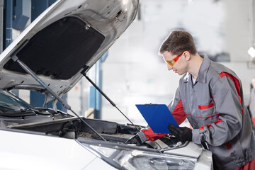 Worker Man mechanic examining car with clipboard in auto repair shop