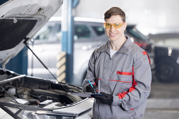Portrait industry worker Caucasian male auto mechanic inspecting car engine in garage