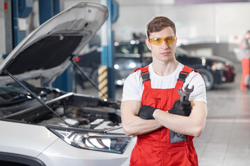 Portrait worker Caucasian male auto mechanic in workshop with open car hood and tools