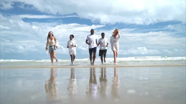 Group of diverse friends having fun at the beach, walking and jump in the waves on a sunny day