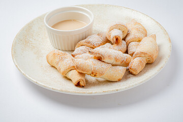 Freshly baked pastries sprinkled with powdered sugar lay on a plate next to a creamy dipping sauce
