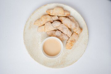 Golden pastry twists dusted with sugar sit elegantly beside a small bowl of creamy dip