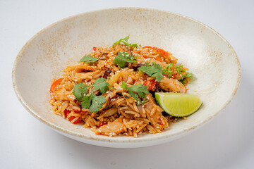 A colorful dish of stir-fried rice garnished with cilantro, vegetables, and a slice of lime