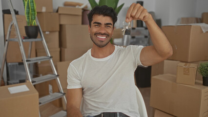 Man holds keys aloft inside a building interior crowded with moving boxes and a ladder; new...