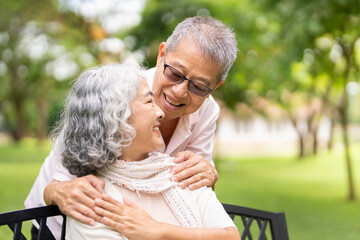 Smiling senior couple embracing and holding hands while resting on  bench in park.