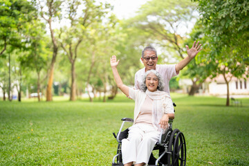 Senior woman in wheelchair walking with old man in park. Elderly family couple. man supporting...