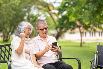 Happy senior couple relaxing together in a city park, sitting on a park bench with  wheelchair is...
