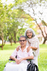 Senior wife takes her disabled husband on a walk through the park.
