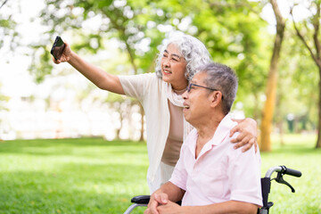 Smiling Senior man Disability in wheelchair with wife in a summer park taking a selfie photo with...