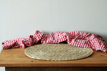 Empty wooden table with wicker placemat and red checkered cloth for product placement