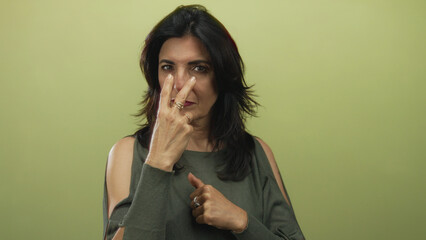 Middle aged woman pointing finger directly at camera in studio against olive green wall with...