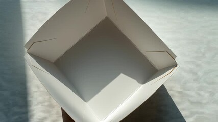A white box with a white lid is sitting on a table. The box is empty and has a shadow on it - Powered by Adobe