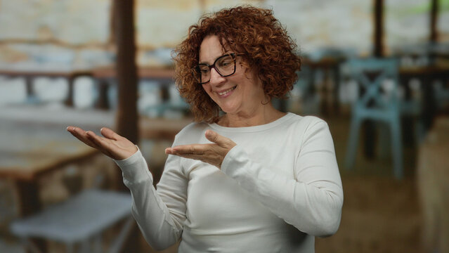 Woman presenting something on a terrace with a smile wearing glasses with curly hair in an outdoor restaurant setting. - Powered by Adobe