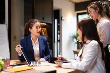 Confident mature business professional woman talking to younger female colleague at office table, speaking, gesturing, teaching, explaining work tasks. Elder mentor training intern.
