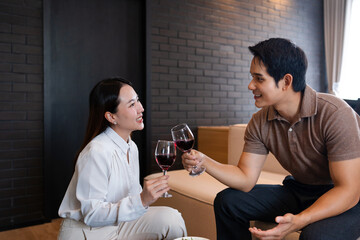 Happy young woman cheering glasses of red wine with smiling man enjoying romantic family time in modern apartment. Married couple spending free weekend time together at home.