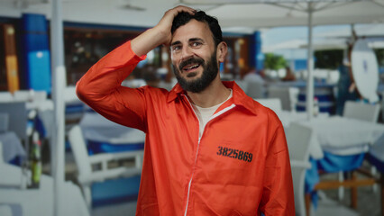 Fototapeta premium Hispanic man in prison jumpsuit smiling in a restaurant setting, surrounded by tables, creating a striking contrast between his attire and the casual dining background.