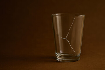 Cracked transparent glass cup on brown background with visible fracture lines