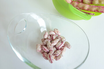 Pink kidney bean pods and beans in glass bowl on kitchen table. Healthy food and vegetables. Organic seasonal farm products.