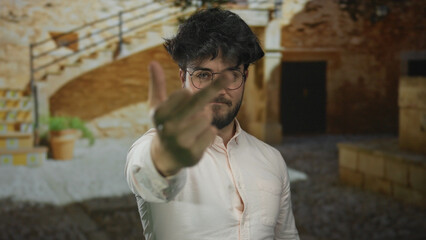 Young bearded man outdoors on sunny day making rude gesture showing middle finger in courtyard with...