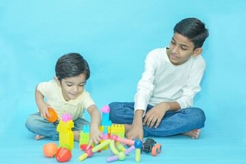 Two Indian kids playing with educational toys together isolated against blue background. Children...