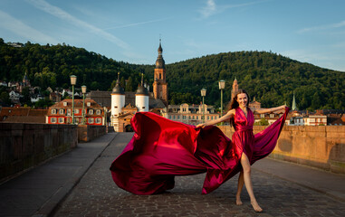 schöne Frau in rotem Kleid genießt die Morgensonne auf der alten Brücke in Heidelberg.