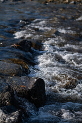 The river rushed over the rocks, creating a spray of mist in the bright sunlight. The spray...