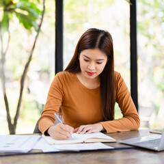 Businesswoman working remotely in a Home office taking notes in a notepad . woman hand writing in an agenda on a desk at home or office.