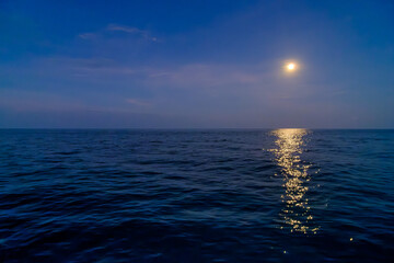 a yellow vivid bright full moon in the blue sky over the open sea