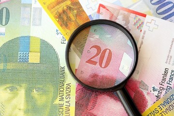 Swiss franc banknotes and magnifying glass. The current francs money bills with loupe lies on table