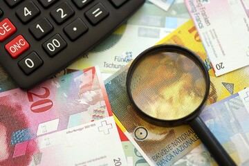 Swiss franc banknotes and calculator with magnifying glass. The current francs money bills and calc