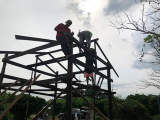 Silhouettes of carpenters on top of the wooden frame are joining girders and beams to construct a...