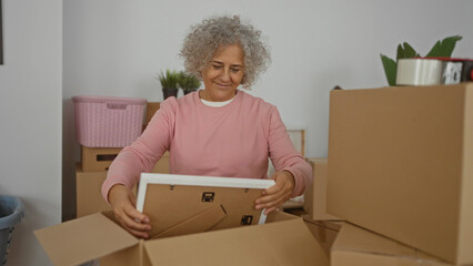 Woman unpacking a picture frame in a new home surrounded by cardboard boxes, reflecting a moment of nostalgia and new beginnings in a cozy indoor setting.